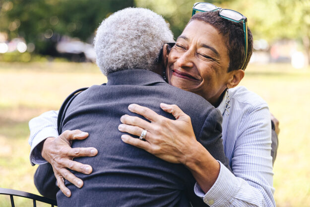 a young woman smiles s she hugs her senior loved one